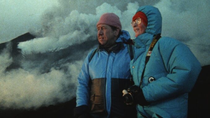 FireOfLove_Film Still 1b_Katia and Maurice Krafft, in blue winter jackets, gaze upon a volcano in the distance as smoke, steam and ash swirl behind them (Credit Image'Est)